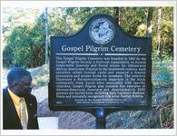 Man stands next to Gospel Pilgrim Cemetery Sign