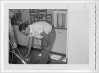 Photograph of two men handling a spray painter inside of a kitchen, Clarkesville, Habersham County, Georgia, 1953