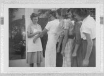 Photograph of a woman examining another woman's arm next to a queue of teenage girls, Clarkesville, Habersham County, Georgia, 1953