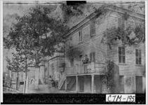 [Photograph of a man on the porch of a house]