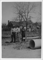 Photograph of three undidentified men observing a clay or concrete pipe, Manchester, Georgia