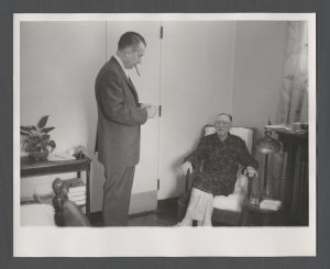 School of Medicine - Man smoking a cigar while talking to a seated elderly man