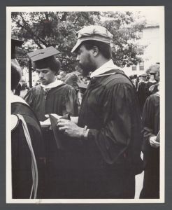 Commencement, 1970s and 1980s - Student stands and holds graduation cap