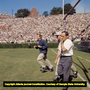 Coach Vince Dooley, assistant coach Bill Dooley and staff run out onto Sanford Stadium's field, 1965