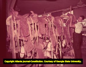Saddle maker stacks up newly finished saddles on racks, 1951