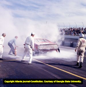 Pit crew members extinguish an automobile fire during a race at the Atlanta Motor Speedway, 1972