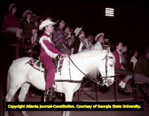 Rodeo performer waits on the sidelines and watches with the audience, 1958