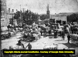 Farmers with wagons of baled cotton convene in a town square, circa 1900s