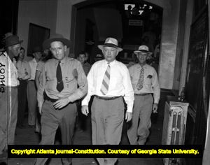 John Wallace on trial for murder escorted by a sheriff through the courthouse, 1948