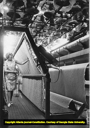 Textile worker inspects a roll of carpet during production, 1971
