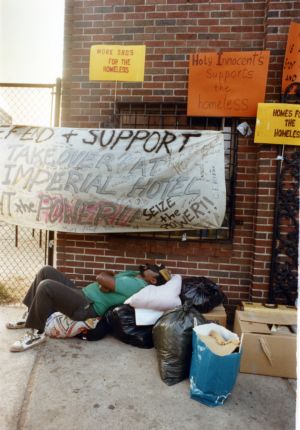 Homeless person waits underneath banners and signs from a demonstration at the Imperial Hotel, 1990