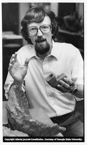 Archaeologist Dr. Roy Dickens poses with soapstone artifacts, 1982