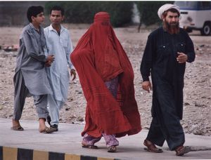 Muslim woman in full burqa walking with three men from her family on a city street, South Asia or Middle East, photograph by Jean Shifrin, 1992.