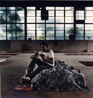 Homeless man, Chip, sitting on his bed while rolling a cigarette at the old MARTA bus repair facility on Piedmont and Pine, Atlanta, now demolished, Gerogia, August 23, 1992.