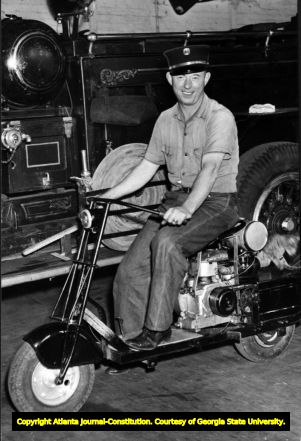 Atlanta fireman Red Adams riding motor scooter, 1942.