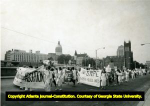 Women's rights demonstration and march, Hunter Street (later, renamed Martin Luther King, Jr. Drive), August 23, 1980. In the background is the Catholic Shrine of the Immaculate Conception (church on the right) and the Georgia State Capitol dome towards the left.