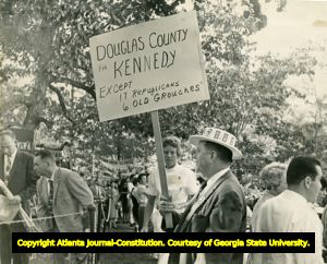John F. Kennedy campaign supporter, carrying sign that reads "Douglas County for Kennedy, except 17 Republicans, 6 old 'grouches'," Warn Springs, Georgia, October 10, 1960.