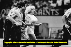 Morganna Roberts, exotic dancer also known as the "Kissing Bandit," being led off the field after kissing New Orleans Saints' quarterback, Mercedes-Benz Superdome, New Orleans, Louisiana, September 7, 1986.