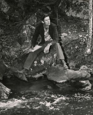 Poet Byron Herbert Reece sitting on the edge of a river with paper and pencil in hand, Georgia, 1950s.