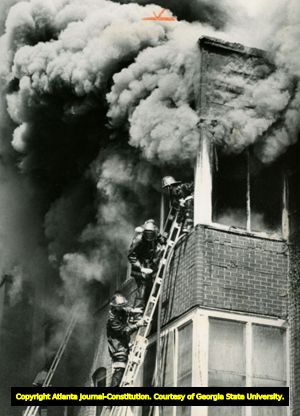 Firemen climb ladder into burning building, Atlanta, Georgia, August 1977.