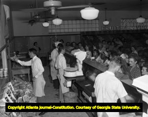 Deli workers behind a counter take orders from a large group of grocery shoppers, 1946