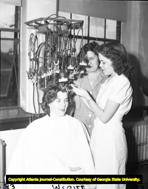 Hairdresser attaches a woman's hair to a perm machine, 1945