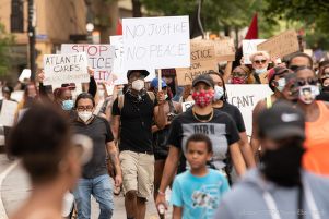 A protester marches with the large crowd holding a sign reading 'No Justice No Peace'