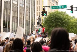 Protesters stand atop the Henry Grady Statue holding up signs