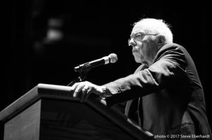 Bernie Sanders looks at the crowd from his podum at a pause in his speech (grayscale)