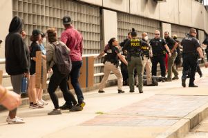 Police Officers surround a man the ground while protesters watch