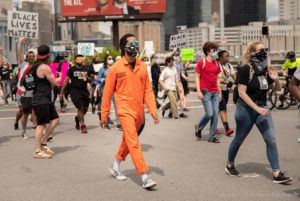 A protester marches through the street wearing an orange prision jumpsuit