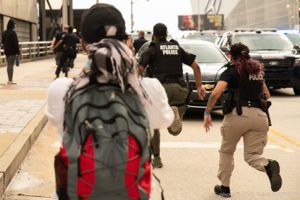 Police Officers go running down the street past protesters and traffic