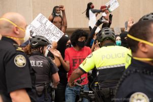 Protesters hold their hands and signs up as they are kept on the sidewalk by officers