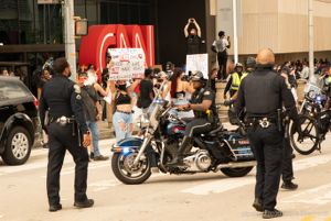 Protesters hold up signs and record events on their phones as Police Officers block off further movement