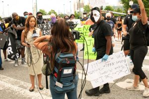 A protester approaches the news reporter and begins to interupt her newscast