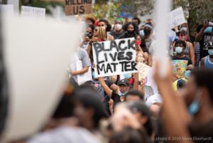 A protester amongst a crowd holds up a sign reading 'Black Lives Matter'