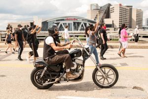 A protester rides a motorcycle alongside protesters, joining the protesters