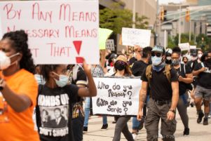 A protester holds up a sign reading 'Who do you protect? Who do you serve?'