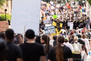 A protester amongst the large crowd holds up a sign reading 'No Justice No Peace'