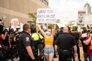 A protester holds up a sign reading 'Would You Kneel on My Neck, Officer? #JusticeForGeorgeFloyd'