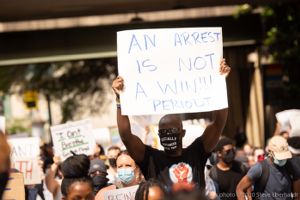 A protester holds up a sign reading 'An Arrest is Not A Win!!! Period'