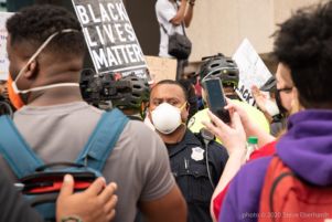 Protesters record a Police Officer as the officer stands there