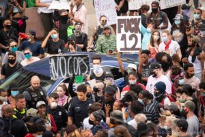 Protesters hold signs in the air reading 'No Cops' and 'F*ck 12'