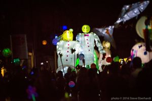 Two paper lantern people are carried through the parade