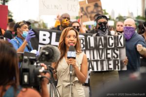 A news reporter continues her report after having her report interupted by a protester