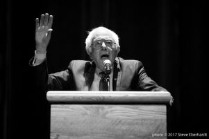 Bernie Sanders speaks to a crowd from his podium (grayscale)