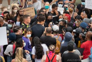 A large crowd of protesters surround police officers, recording them as well