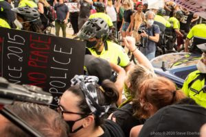Police Officers begin to push protesters to the side of the street to let other officers and vehicles through the crowd