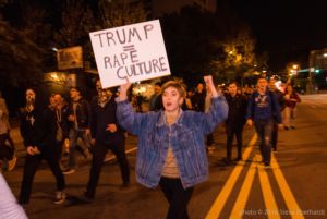 A protester marches holding a 'Trump=Rape Culture' sign