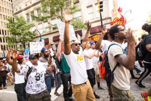 Protesters march down the street holding their hands and signs in the air